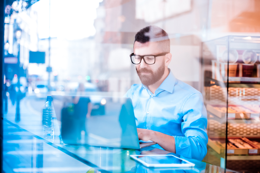 Hipster manager in cafe, working on laptop by window